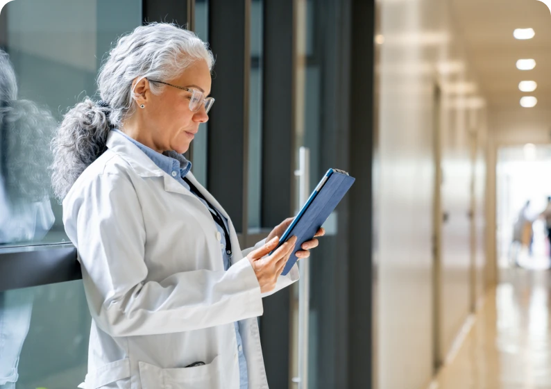 Doctor reading tablet in hospital hallway.
